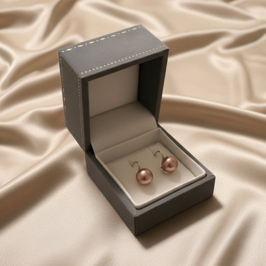 Rose gold earrings in a jewelry box held by a hand on a beige fabric background